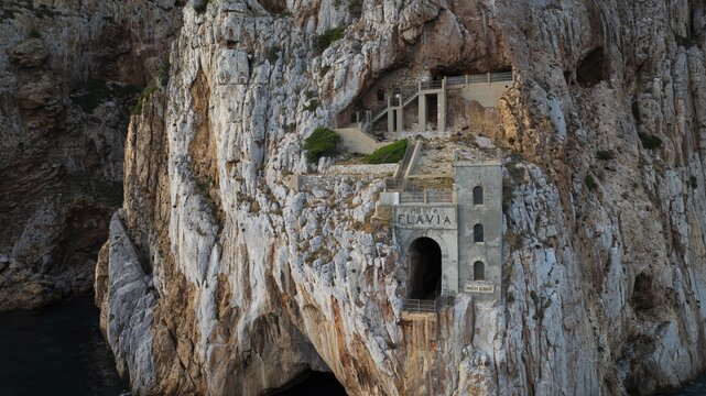 Aerial view of the old mine building carved into the cliffside, a stark contrast against the azure sea, Masua, Sardegna, Italy.