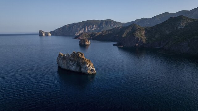 Aerial view of rugged rock formations rise majestically from the deep blue sea near the coastline, a serene landscape of natural beauty, Masua, Sardegna, Italy.