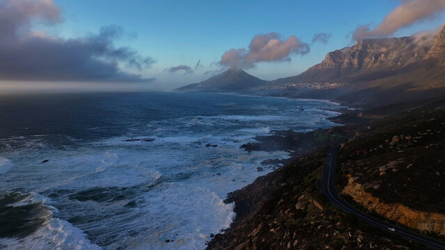 Aerial view of the dramatic coastline where the churning ocean meets the rugged cliffs beneath a sky of brooding clouds, Cape Town, Western Cape, South Africa.
