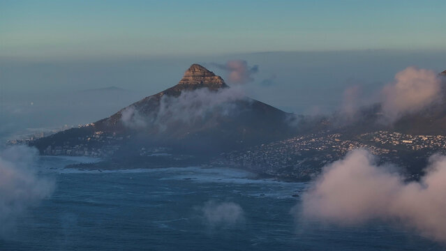 Aerial view of Lion's Head peak shrouded in ethereal mist, kissing the sea and sky in a dance of light and shadow, Cape Town, Western Cape, South Africa.