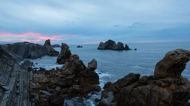 Aerial view of jagged cliffs and dramatic rock formations meet the turbulent sea under a twilight sky, Donostia San Sebastian, Basque Country, Spain.