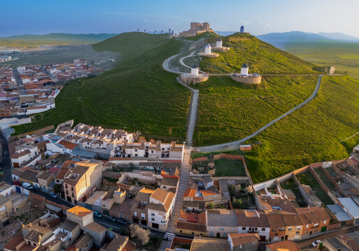 Aerial view of windmills standing guard on the verdant hill, overlooking the terracotta rooftops of the ancient town, Consuegra, Castile-La Mancha, Spain.