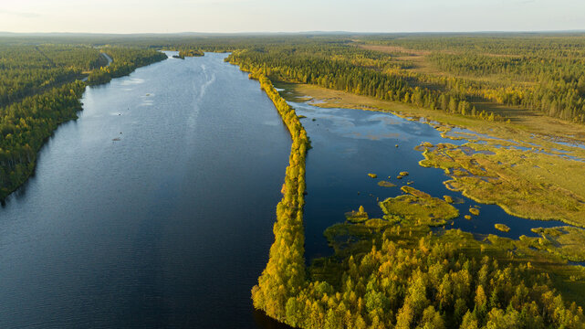 Aerial view of the winding river reflecting the sky, bordered by the forest in vibrant autumn colors, Sodankyla, Lapland, Finland.