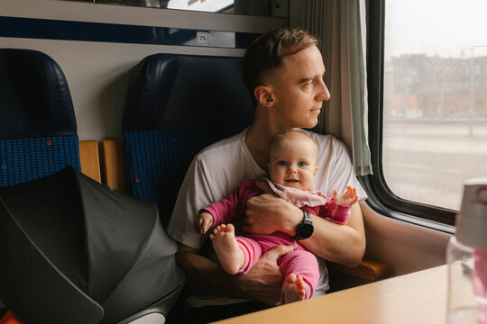 Father holding baby on public transport train looking out window