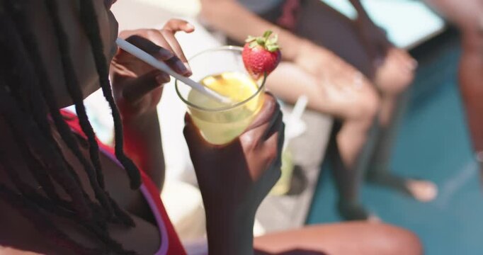 Hand is reaching and stirring clear cup with white straw and strawberry at poolside for sipping