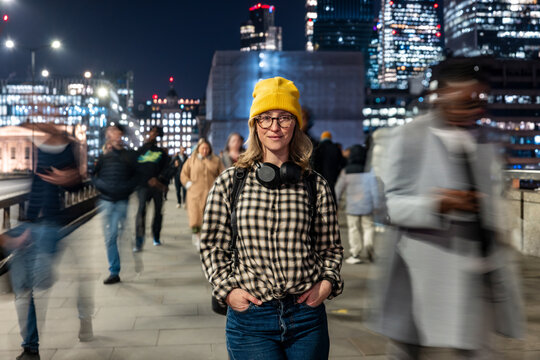 Urban commuter with headphones and yellow hat on London bridge at night