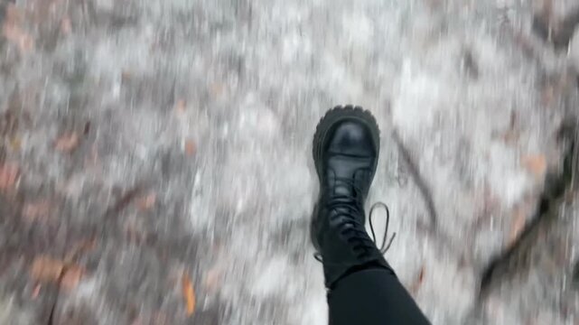 Icy path with compacted snow and slippery surface, cautious boots stepping carefully, muted winter park setting, close POV of tread Taken on mobile device.