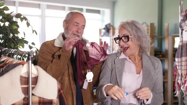 Mature couple spend time in shop and choose bra lingerie set. Changing wardrobe, shaping style of clothing. Designer clothes, clothing of world brands