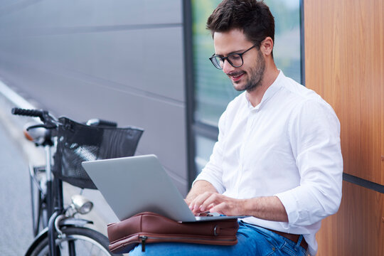Businessman with bicycle using laptop outdoors