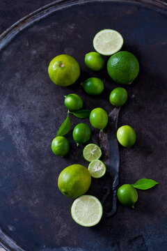 Sliced and whole limequats, limes, leaves and old knife on dark ground