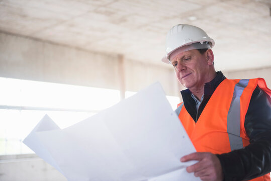 Man with plan wearing safety vest in building under construction