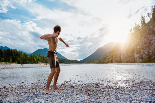 Germany, Bavaria, man standing at riverside throwing stone