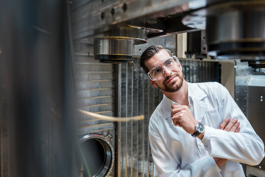 Man wearing lab coat and safety goggles at machine