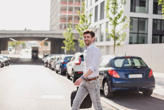 Smiling businessman with laptop bag in the city crossing the street