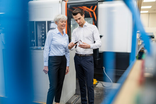 Businessman and senior businesswoman measuring workpiece in a factory