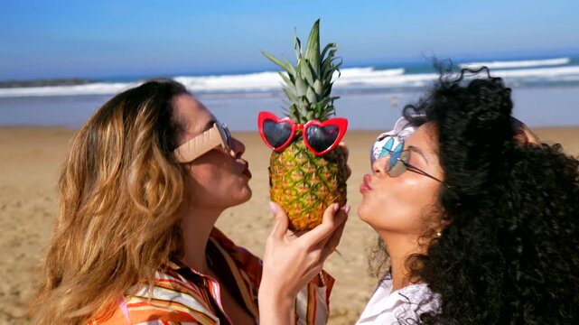 Two cheerful friends having fun with pineapple on the beach