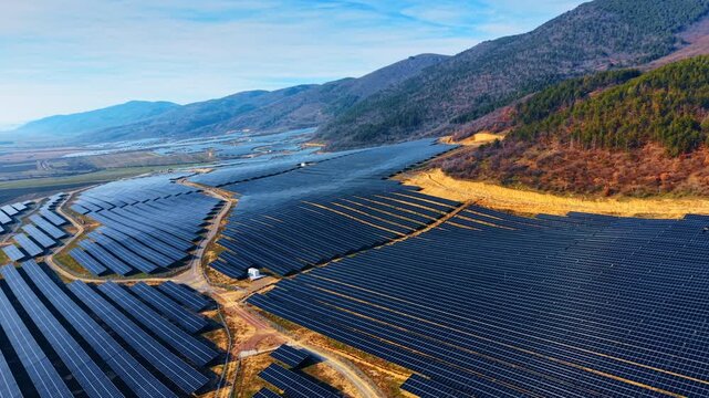 Aerial view of solar panel farm in mountain valley. Wide high angle shot of photovoltaic power plant installed on hills under blue sky and sunlight.