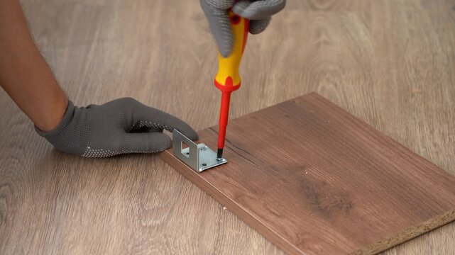 Close up of hands assemble wooden shelf using screwdriver. Process of assembling furniture. Furniture assembler installs fasteners