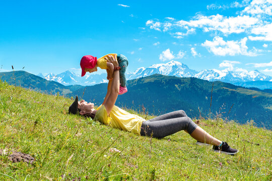 Mother picking up baby girl while lying on grass at Col des Aravis, Haute-Savoie, France