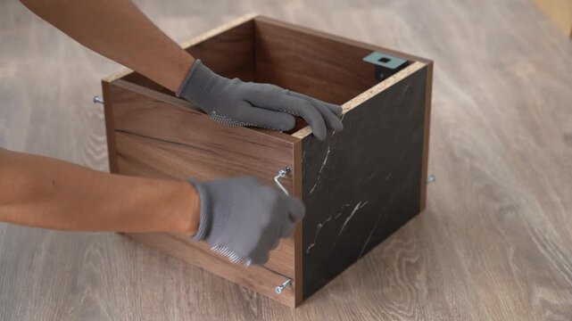 Male hands assemble wooden shelf using screwdriver at home. Process of assembling furniture. Furniture assembler installs fasteners