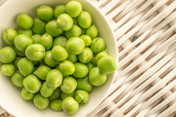 Green fresh peas on a mat woven from vines, macro. Top view.