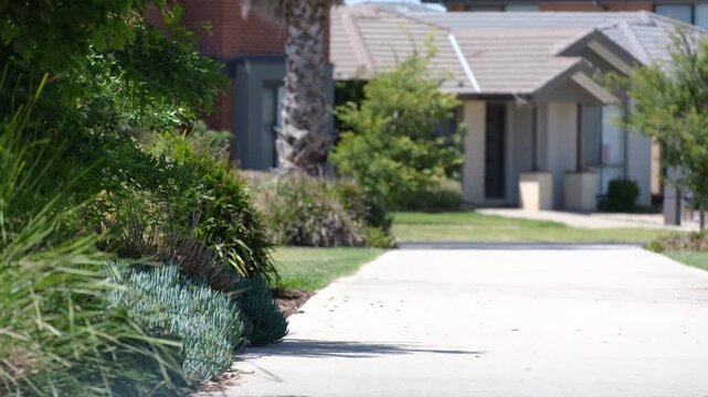 Sunlit suburban footpath in an Australian neighborhood lined with drought-tolerant landscaping and modern houses. Dry climate of a residential areas, heatwaves on a quiet local street