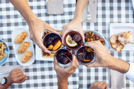 Hands of friends toasting vermouth at table in cafe