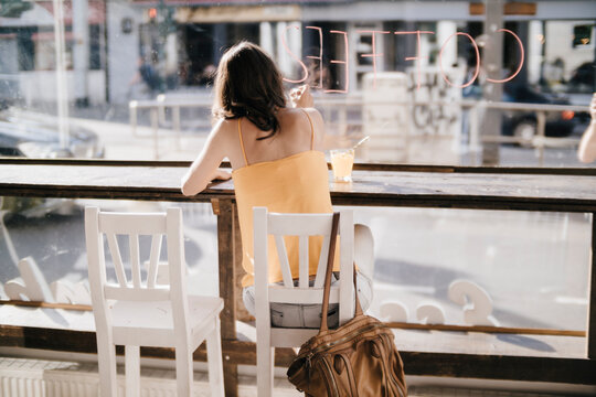 Woman sitting in cafe, writing the word 'coffee' on window pane