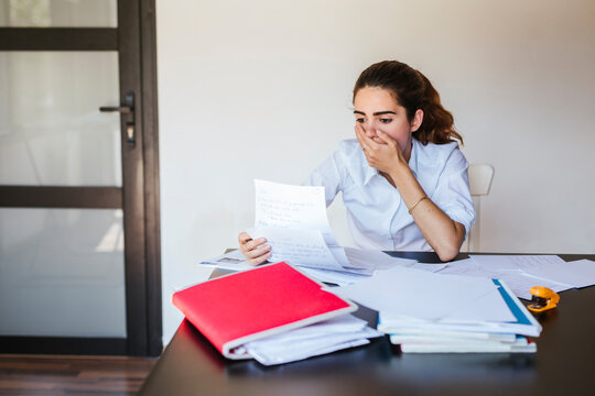 Shocked female student reading document at desk at home