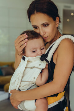 Mother carrying her baby girl in sling at home