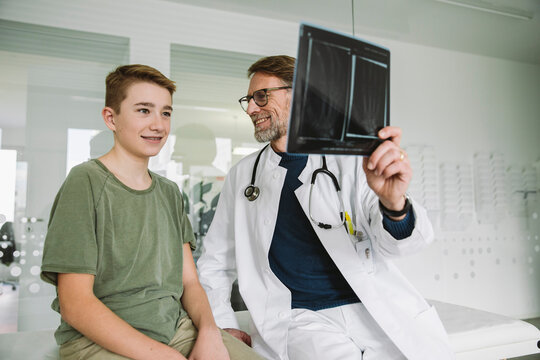 Doctor explaining x-ray image of broken hand to teenage boy in medical practice