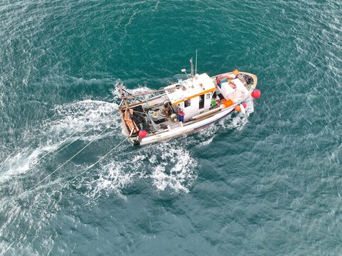Aerial view of a fishing boat cuts through the cerulean sea, its wake a frothy white against the deep blue, Cornwall, United Kingdom.