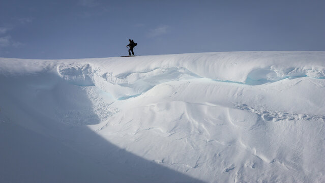 Aerial view of a lone snowboarder silhouetted against the sky on a snow-covered mountain ridge, Colomby de Gex, Echenevex, Auvergne-Rhone-Alpes, France.