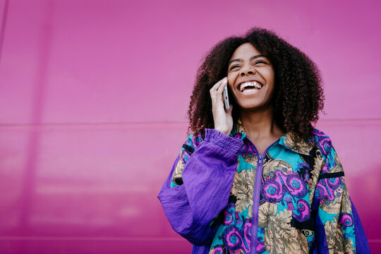 Smiling woman talking on the phone, pink wall in the background