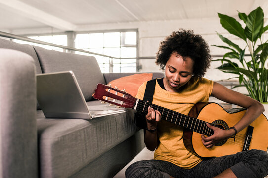 Young woman at home with laptop playing guitar