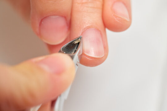 Hand getting a manicure, a technician carefully removing dead cuticles and skin from fingernail