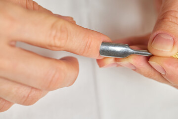 Woman performing a self-care manicure, pushing back cuticles on her nails