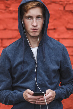 Young man with cell phone and earphones at red brick wall
