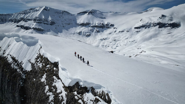Aerial view of a group of ski tourers traversing the snowy expanse near the craggy cliffs of the Gemmi Pass, Leukerbad, Valais, Switzerland.
