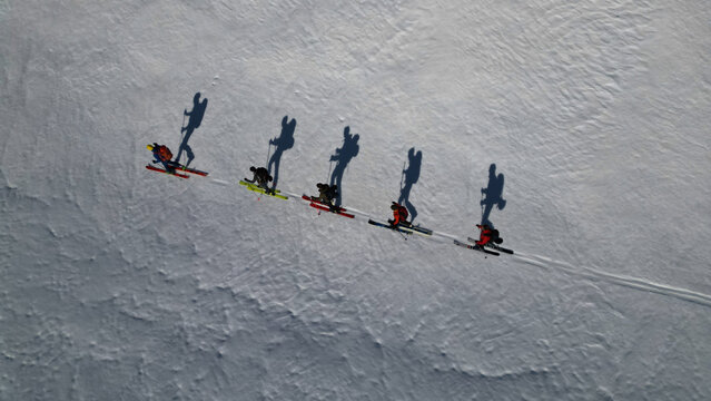 Aerial view of five skiers casting long shadows on the pristine, snow-covered slopes of Leukerbad, Valais, Switzerland.