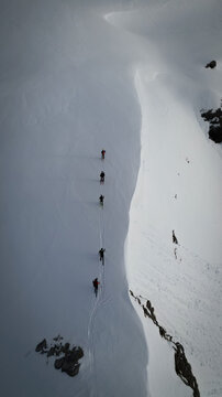Aerial view of silhouetted ski tourers traversing a stark, snow-covered mountain ridge, their tracks etching a path through the pristine white landscape, Leukerbad, Valais, Switzerland.