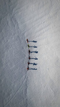 Aerial view of a line of skiers casting long shadows on the pristine white snow, Leukerbad, Valais, Switzerland.