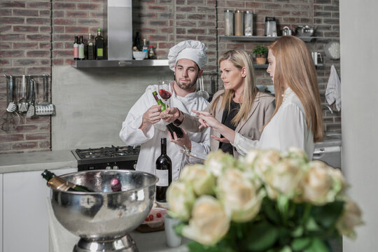 Chef with two women in kitchen tasting wine