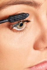 Woman applying black mascara on her eyelashes, focusing on beauty and cosmetics