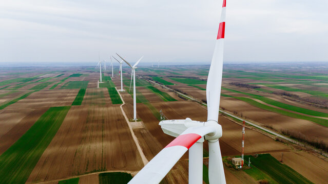 Aerial view of wind turbines standing tall against the patchwork fields, a symphony of green and brown under a muted sky, Alibunar, Vojvodina, Serbia.