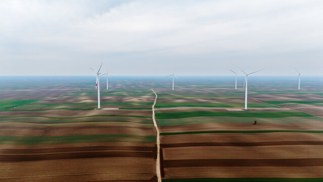 Aerial view of wind turbines standing tall over the patchwork quilt of arable fields, a testament to renewable energy, Alibunar, Vojvodina, Serbia.
