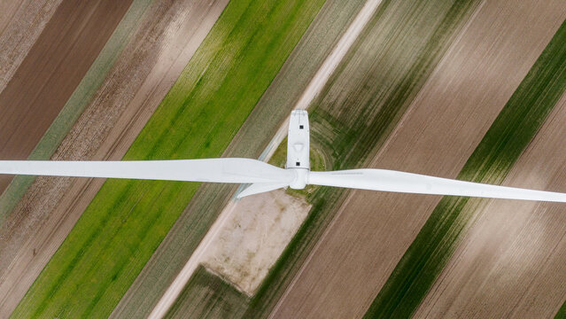 Aerial view of a modern wind turbine's stark white blades contrasting with the patchwork of brown and green fields, Alibunar, Vojvodina, Serbia.