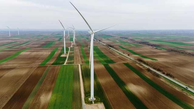 Aerial view of towering wind turbines standing tall amidst the patchwork of brown and green fields, creating a striking contrast against the horizon, Alibunar, Vojvodina, Serbia.