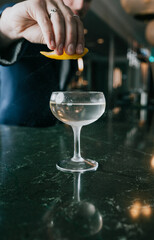 Obraz premium Hand squeezes citrus over cocktail glass. Dark bar counter reflects drink. Warm lighting highlights action. Bartender prepares refreshing drink. Perfect for ads, menus, or lifestyle content