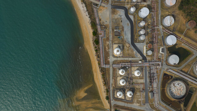 Aerial view of the industrial zone contrasting with the turquoise sea and sandy beach, creating a stark juxtaposition of nature and industry, Thung Sukhla, Chon Buri, Thailand.